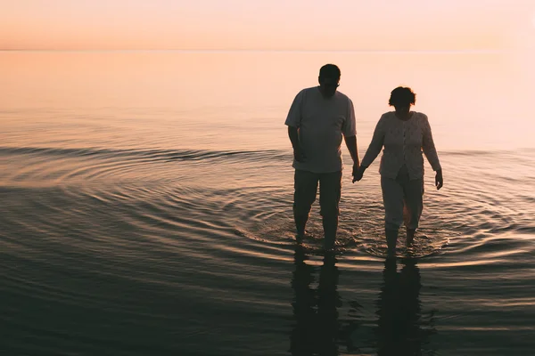 Silhouette eines erwachsenen Paares, das im Meer vor einem Sonnenuntergang steht. — Stockfoto