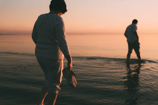 Adult married couple holds shoes in hand and walks on water. — Stock Photo, Image