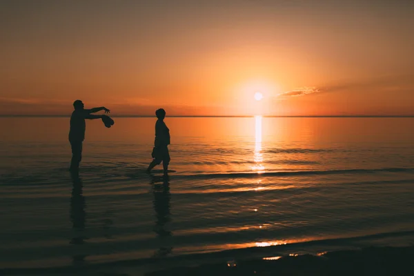 Silhouette eines erwachsenen Paares, das im Meer lebt und Schuhe in der Hand hält. — Stockfoto
