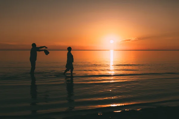 Silhouet van volwassen paar die kost in de zee en in de hand houdt van schoeisel. — Stockfoto