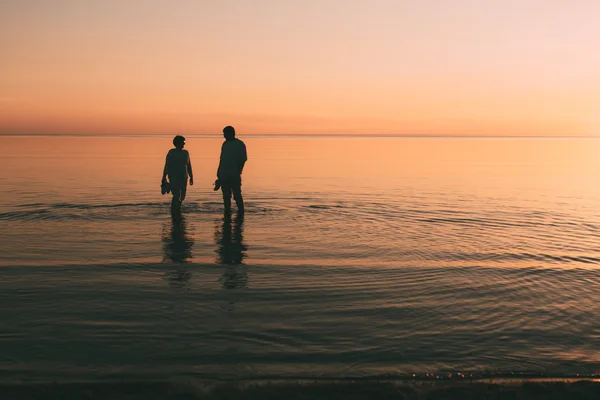 Silhouette eines erwachsenen Paares, das im Meer lebt und Schuhe in der Hand hält. — Stockfoto