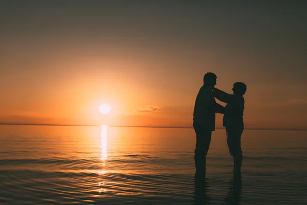 Silhouet van volwassen paar staande in de zee tegen een zonsondergang. — Stockfoto