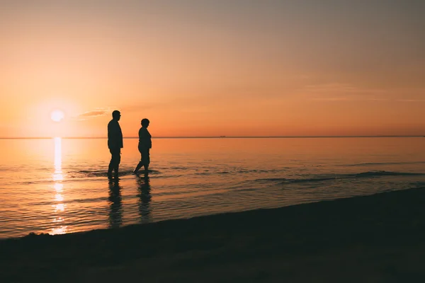 Silueta de pareja adulta de pie en el mar contra una puesta de sol . — Foto de Stock