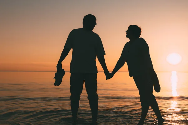 Silueta dospělého páru stojící v moři proti západu slunce. — Stock fotografie
