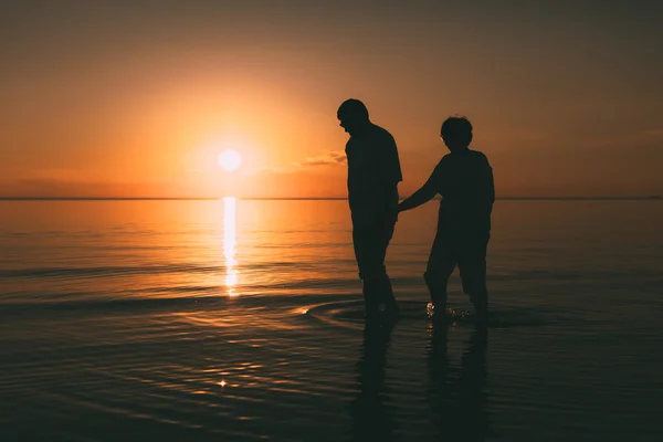 Silhouet van volwassen paar staande in de zee tegen een zonsondergang. — Stockfoto
