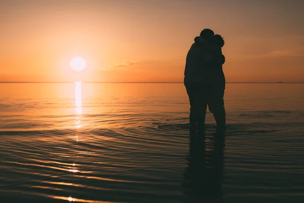 Silueta de pareja adulta de pie en el mar contra una puesta de sol . — Foto de Stock