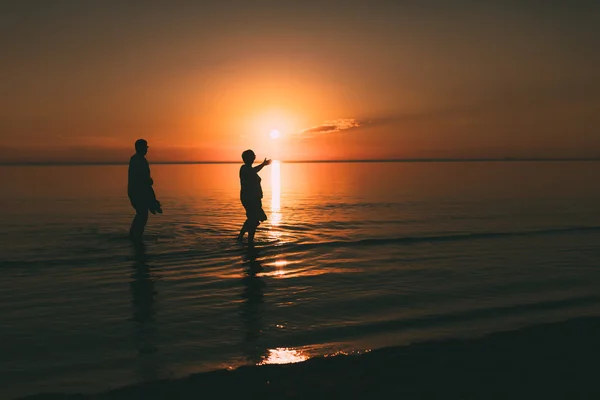 Silhouette eines erwachsenen Paares, das im Meer lebt und Schuhe in der Hand hält. — Stockfoto