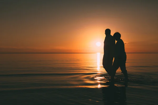 Silhouette eines erwachsenen Paares, das im Meer vor einem Sonnenuntergang steht. — Stockfoto