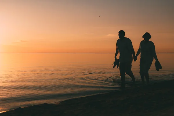 Silueta de pareja adulta camina en la orilla del mar contra una puesta de sol . — Foto de Stock