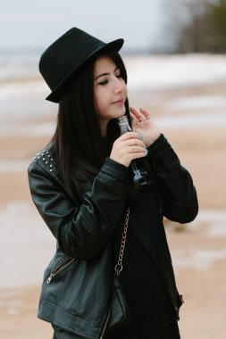 Genç Yetişkin güzel esmer kadın siyah elbise ve siyah şapka elinde içki ile cam şişe tutan.