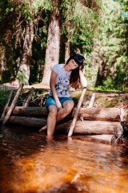 Günlükleri üzerinde oturan ve ayaklarının ırmağa indirdi genç kadın.