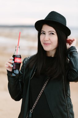 Siyah elbise ve siyah şapka coca cola içmek tutan genç yetişkin güzel esmer kadın.