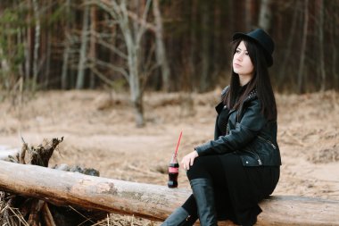 Coca cola şişesi yanında bir bankta oturan genç kadın.
