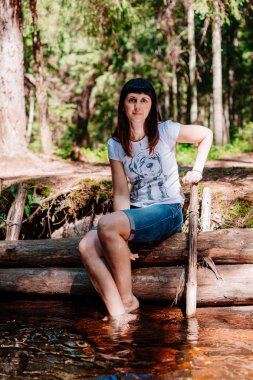 Günlükleri üzerinde oturan ve ayaklarının ırmağa indirdi genç kadın.