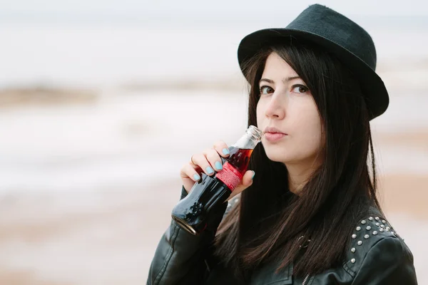 Junge Erwachsene schöne brünette Frau in schwarzem Kleid und schwarzem Hut mit einem Getränk Coca Cola. — Stockfoto