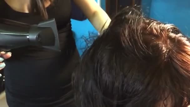 Cabeleireiro seca o cabelo ao cliente e empilha-os por meio do secador de cabelo e uma escova de cabelo . — Vídeo de Stock