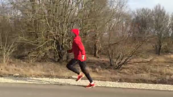 Sportsman in red clothes runs on the park alley the camera follows him. — Stock Video