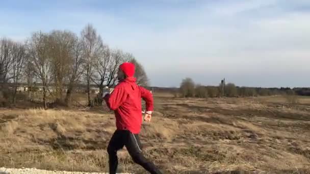 Sportowca w czerwone ubrania działa na parkowej, że kamera podąża za nim. — Wideo stockowe
