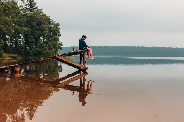 Man sits on a wooden bridge waits when the fish are biting. — Stock Photo, Image