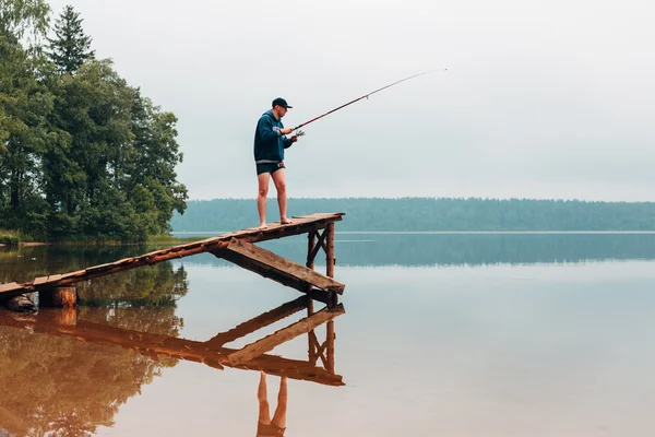Mann zieht Angelrute auf Holzbrücke. — Stockfoto