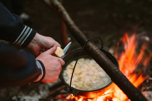 Fish soup cooking on fire in nature and the human hands cut potatoes in a pan. — Stock Photo, Image