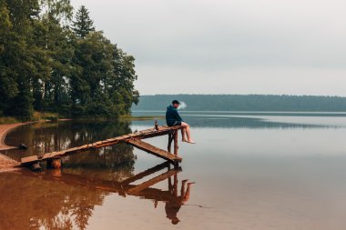 Adam oturur bir ahşap köprü bekler ne zaman balık ısırma ve Sigara.