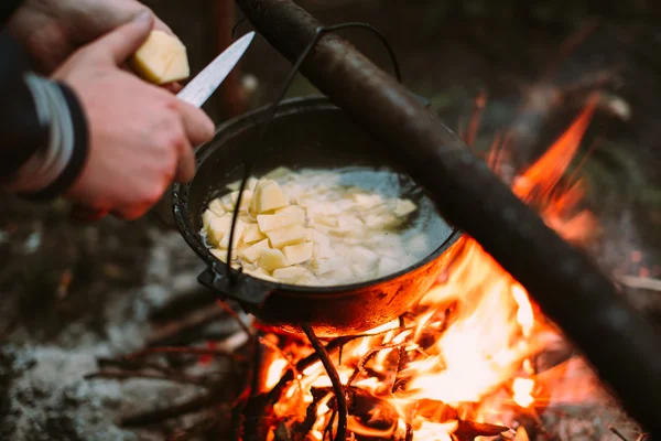 Fischsuppe in der Natur am Feuer kochen und die menschlichen Hände Kartoffeln in einer Pfanne schneiden. — Stockfoto