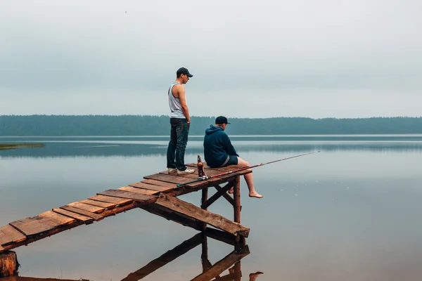 Dos hombres están esperando en un puente de madera cuando los peces están mordiendo . — Foto de Stock