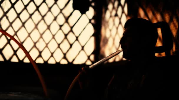Silueta muže kouří vodní dýmky a nechá se kouř. — Stock video