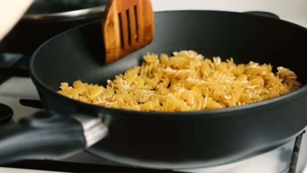 Houten schop roert macaroni in een koekenpan. — Stockvideo