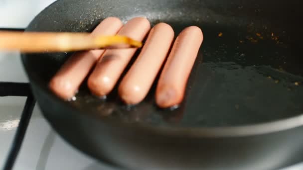 Wooden paddle moves sausages in a pan. — Stock Video