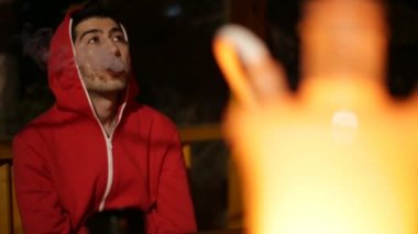 Kamera sağdan sola hareket eder ve bir kukuleta ile kırmızı giysili adam geceleri bir ahşap çardak oturur ve yavaş yavaş bir nargile bir duman exhales kaldırır.