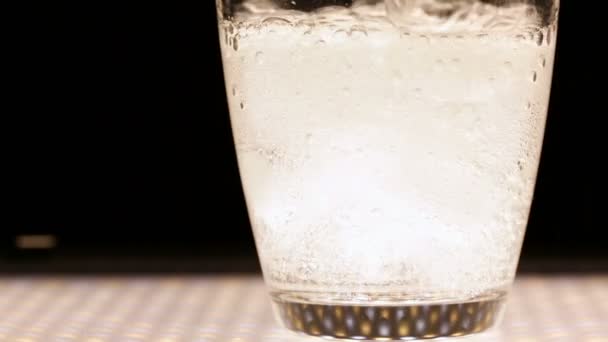 Into a glass with ice pour mineral water on a black background. — Stock Video