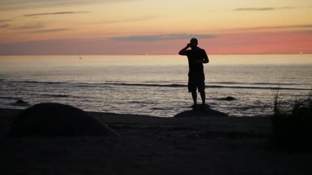 Ember beszél a telefonon, a strandon. Sziluett naplementekor — Stock videók