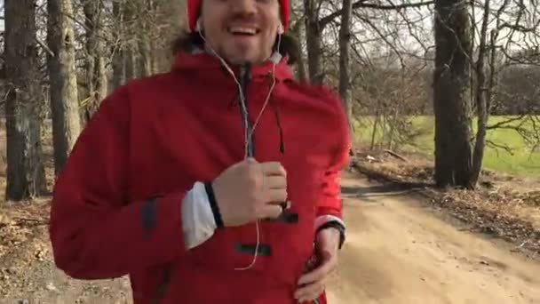 Man in rode kleding loopt op de steeg van het park dat de camera volgt hem. — Stockvideo