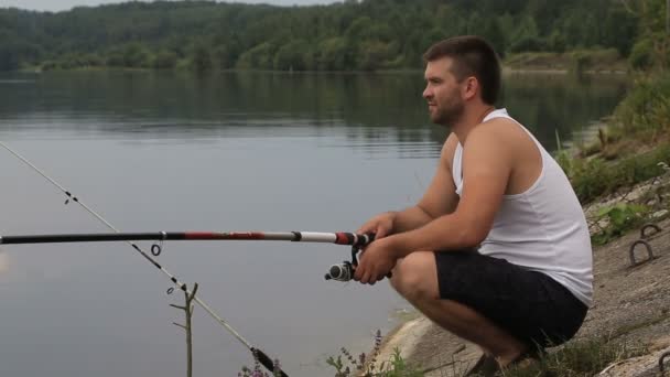 Молодой человек рыбачит на берегу — стоковое видео