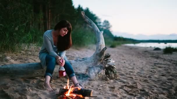 火のキャンプの近くに座っている孤独な少女 — ストック動画