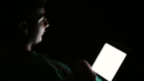 Młody człowiek, przy użyciu komputera tablet cyfrowy w ciemnym pokoju i mówi. — Wideo stockowe