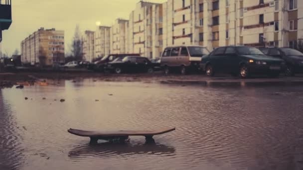Παλιά skateboard σε μια βρώμικη λακκούβα σε φόντο πολλαπλών ορόφων κτίριο και αυτοκίνητα. — Αρχείο Βίντεο