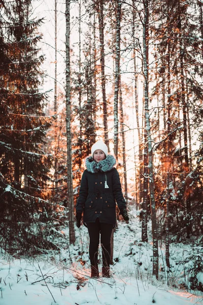 Söt flicka i en vit hatt och en jacka på en bakgrund av en vinter skog. — Stockfoto