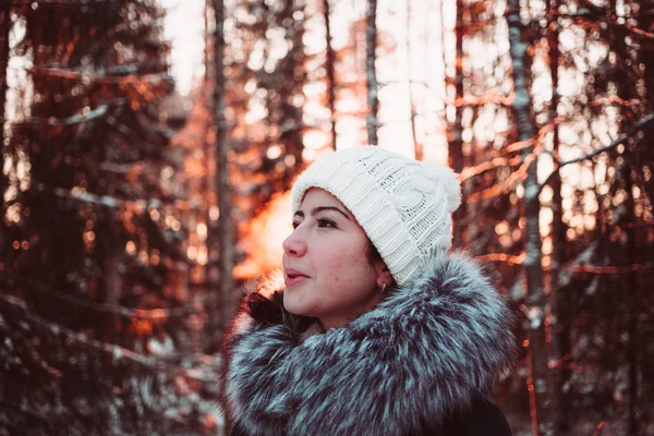 Pretty girl in a white cap and a jacket on a background of a winter forest. — Stock Photo, Image