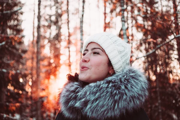 Söt flicka i en vit mössa och en jacka på en bakgrund av en vinter skog. — Stockfoto