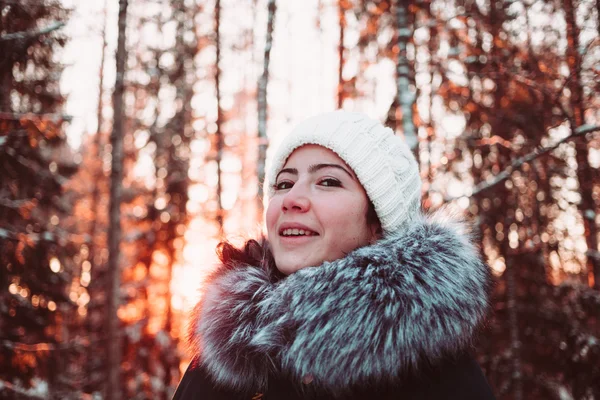 Pretty girl in a white cap and a jacket on a background of a winter forest. — Stock Photo, Image