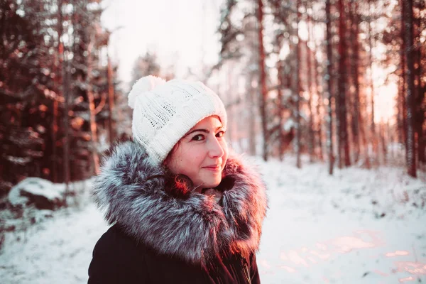 Girl in a white hat and a jacket on a background of a winter forest. — Stock Photo, Image