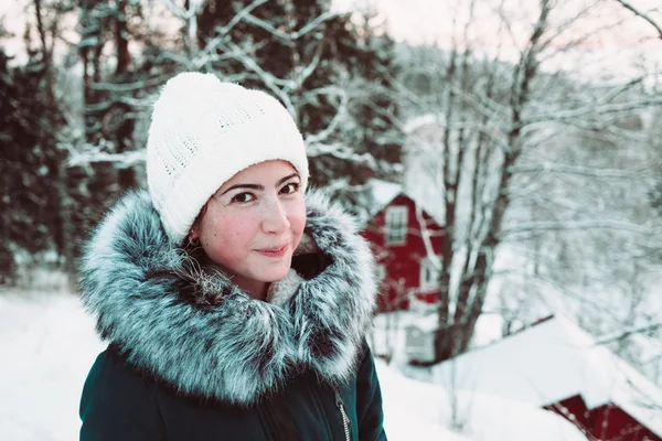 Beautiful young woman in a white cap and a jacket on a background of a winter forest. — Stock Photo, Image