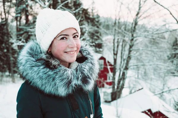 Beautiful young woman in a white cap and a jacket on a background of a winter forest. — Stock Photo, Image