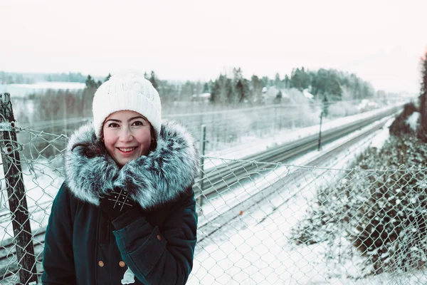 Beautiful girl in a white hat and a jacket on a background of a winter rails. — Stock Photo, Image