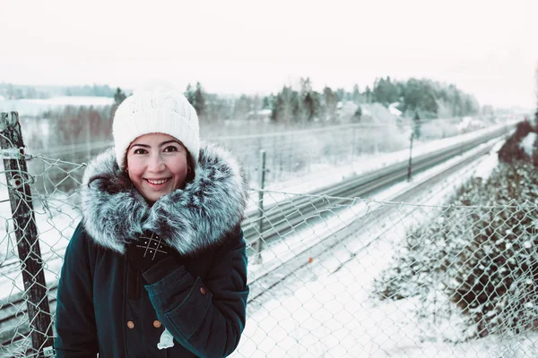 Beautiful girl in a white hat and a jacket on a background of a winter rails. — Stock Photo, Image