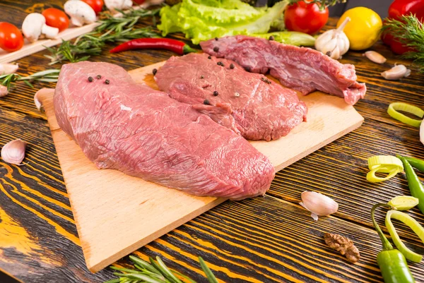 Morceaux de viande crue sur planche et table en bois — Photo
