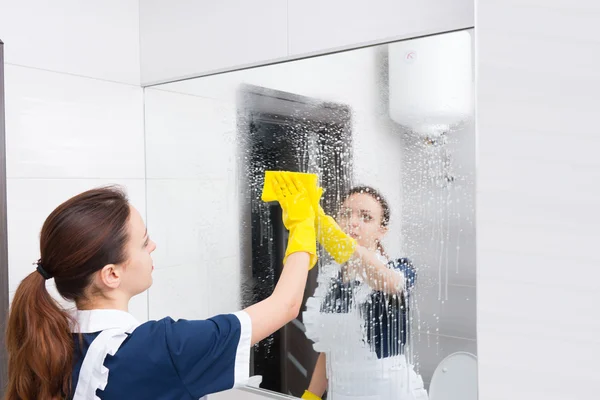 Housekeeper or maid cleaning a large wall mirror — Stock Photo, Image